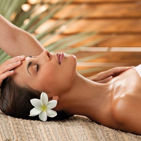 Client enjoying a relaxing spa treatment, lying on a mat with a flower in her hair, embodying tranquility and satisfaction